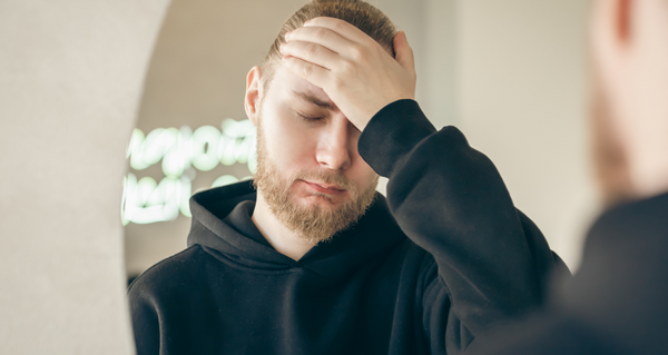 A man with one hand on his forehead frowning.